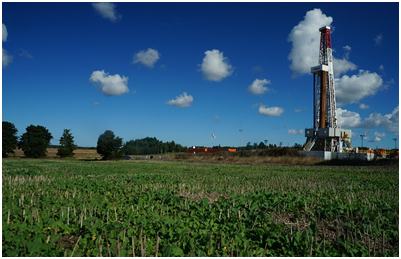 An oil rig in the middle of the field on a cloudless day.